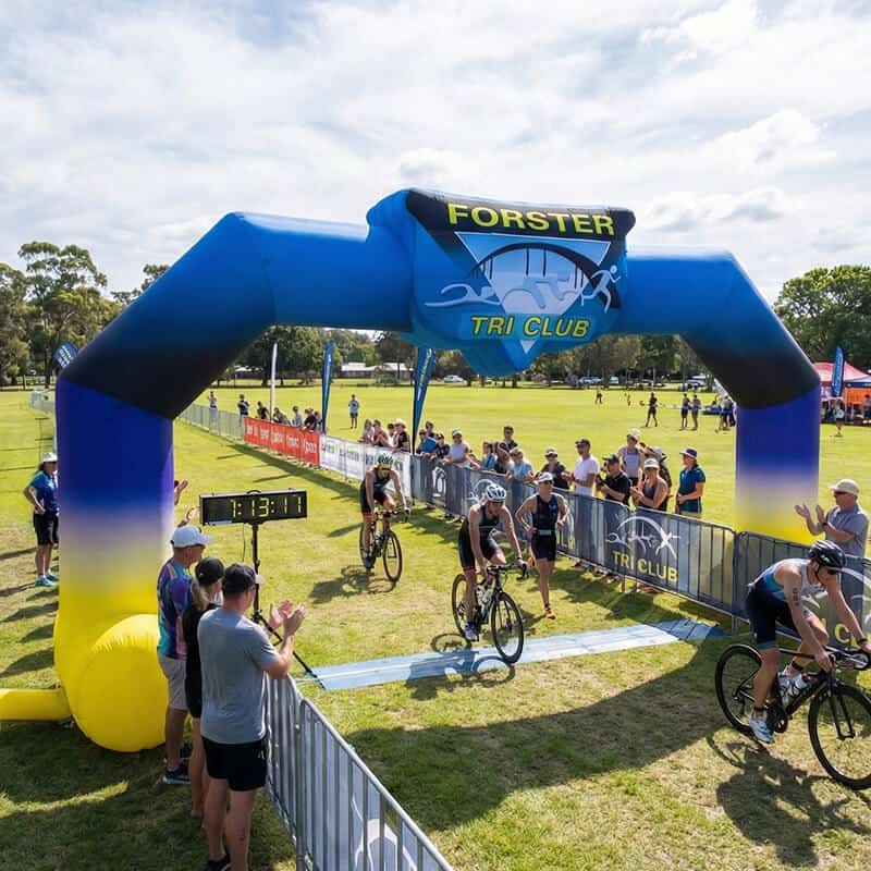 Cyclists riding through Forster tri club inflatable archway